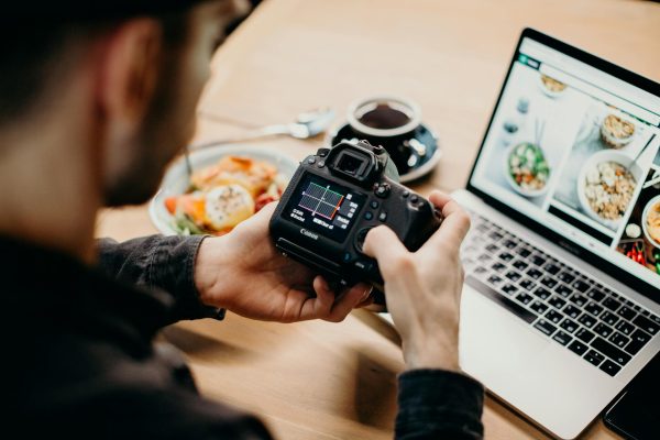 A man reviews photo settings on a camera while working on a laptop in a cozy workspace.