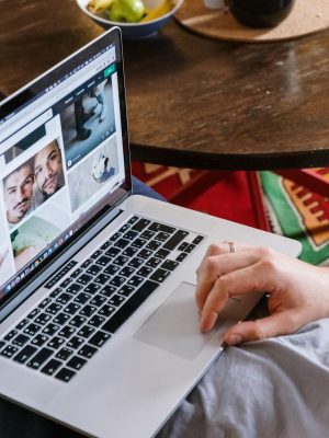 A person uses a laptop to browse photos online, sitting at a wooden table.