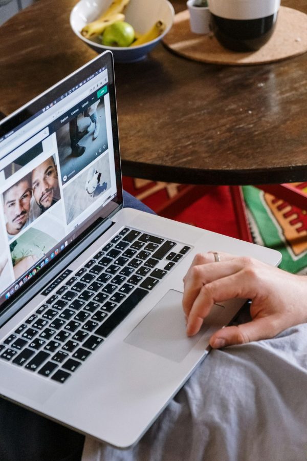 A person uses a laptop to browse photos online, sitting at a wooden table.