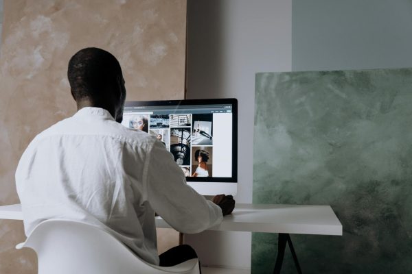 Back view of a man sitting at a computer, browsing images in a modern workspace.