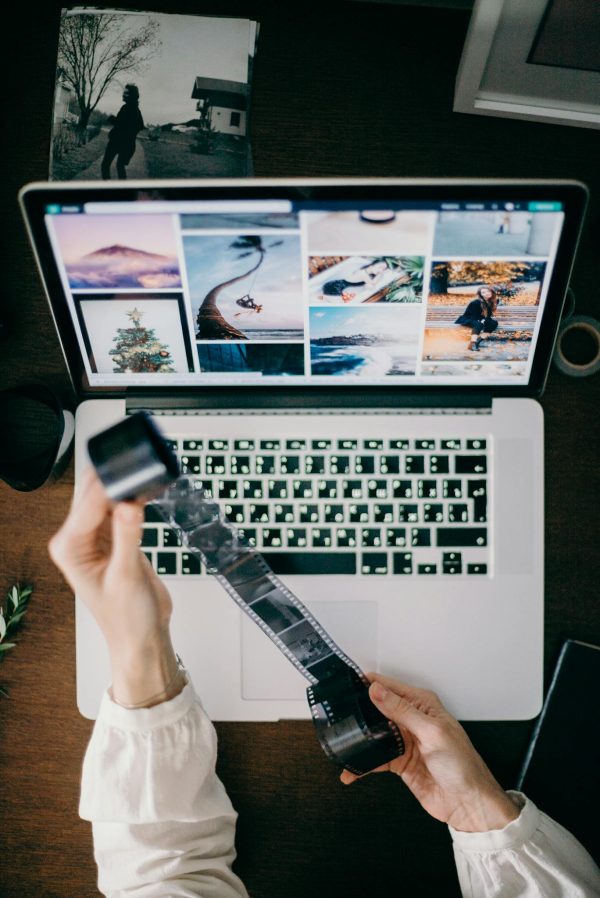 Person holding film strip over laptop showcasing photography work.